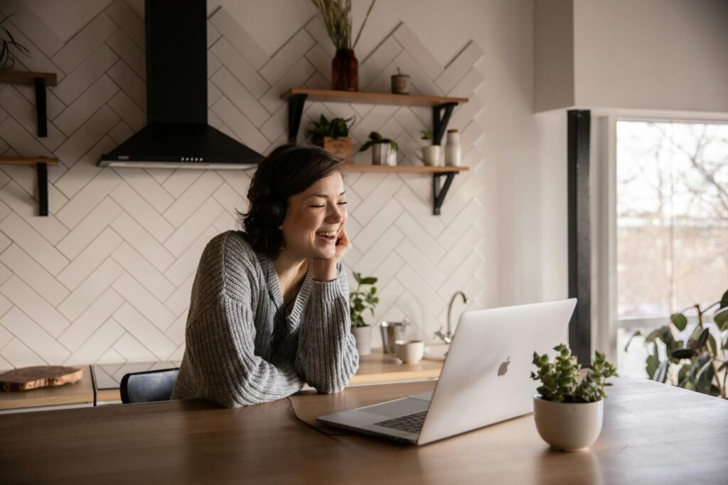 pexels-photo-4049992-4049992 Young cheerful female smiling and talking via laptop while sitting at wooden table in cozy kitchen